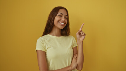 Fototapeta premium Beautiful african american woman smiling and pointing with finger over isolated yellow background