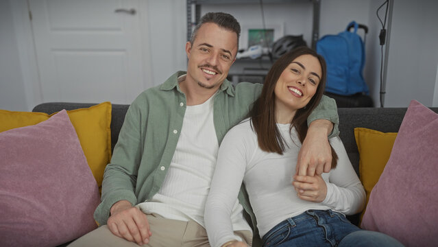 A smiling couple sits closely on a sofa in their modern living room, portraying affection and comfort.