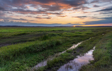A field with a road in the middle and a sunset in the background