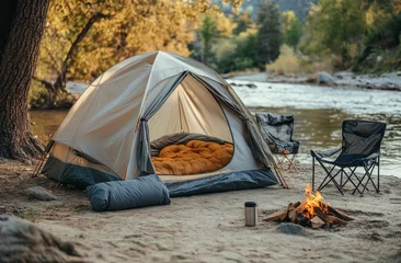 Fotobehang Cozy camping setup beside a river at dusk with a warm fire and comfortable seating © homeganko