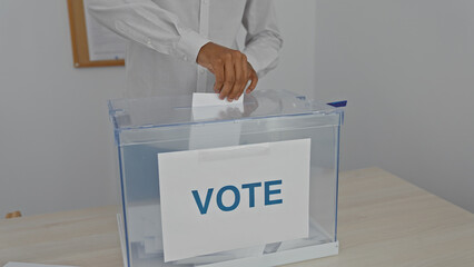 A young black man casts his ballot in a modern electoral room with a clear ballot box marked 'vote'.