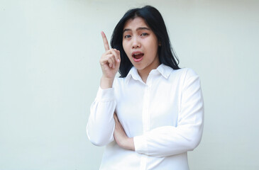 carefree asian young business woman pointing up to empty space with arms folded looking camera surprised show wow expression wearing white formal suit shirt isolated on white background