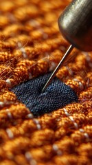 Close-up of a sewing needle stitching through fabric, orange textile background.