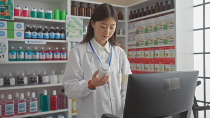 A young asian woman pharmacist examines medication in a modern drugstore with shelves of products.