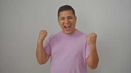 A cheerful young hispanic man celebrates a victory, fist-pumping in triumph against a white background.