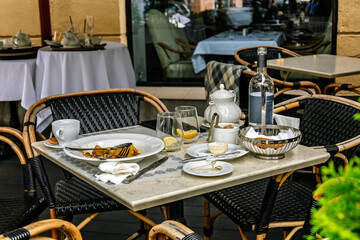 Mess on the table with teapot, mug, glasses, plate after dinner. Dirty dishes on the table. Delicious dinner in restaurant. Leftover food in white plate. Empty dishes and crumbs on table after eating.