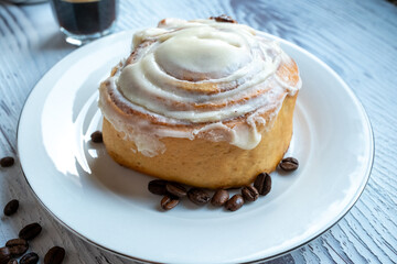 Cinnamon roll on a plate on a wooden background with a glass of espresso next to it