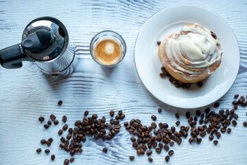 Cinnamon roll on a plate on a wooden background with a glass of espresso next to it