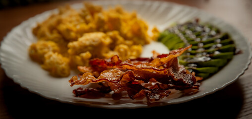 fried bacon close-up on a plate, scrambled eggs and avocado in the background