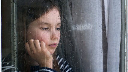 Caucasian little girl looking out window rainy weather dropping sadness anxiety stress crisis...