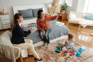 Social worker talking to woman while her daughter playing with toys in the room