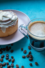 Cinnamon roll on a plate on a wooden background with a glass of espresso next to it