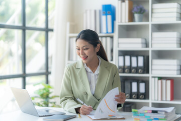 Confident Businesswoman Analyzing Data: A professional woman in a modern office setting, confidently reviewing documents while working on her laptop, radiating an aura of success and focus.  