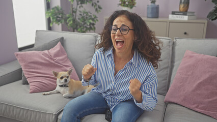 Excited woman cheering on couch with a chihuahua watching tv at home.