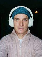 Selfie portrait of a handsome 40-year-old man in headphones, hat and sweater