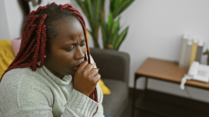 Coughing african american woman with braids at home, showing illness and discomfort indoors.