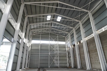 Industrial hangar with a metal frame. High steel columns and beams support the roof made of metal profiles. The interior walls are covered with metal panels.