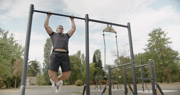 Strong man performs pull-ups on parallel bars in the park, enjoying an outdoor calisthenics workout on a bright, sunny day.