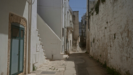 Scenic narrow alley with whitewashed buildings in ostuni, puglia, italy, featuring iconic stone walls, steps, and a clear blue sky.