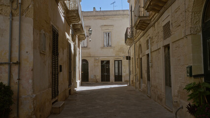 Historic narrow street in lecce, puglia, showcasing old stone buildings with shuttered windows and balconies under the bright european sky