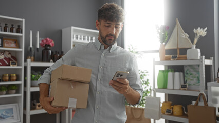 Young man holding boxes and using phone in a home decor store with various decorations and items on...
