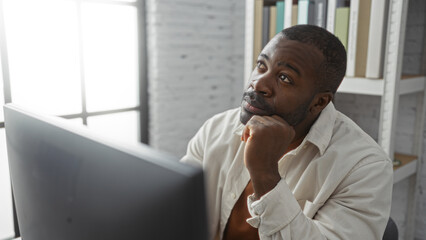 Young man in an office thinks deeply while looking at a computer monitor, suggesting contemplation...