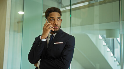 African american man talking on phone in modern office interior, wearing suit and looking focused.