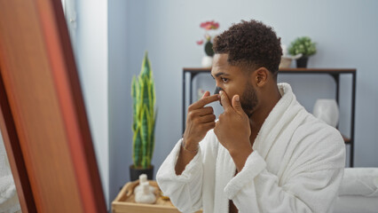 Young man applies a nasal strip in a spa room, dressed in a white robe, standing near a mirror,...