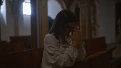A young hispanic woman is praying solemnly inside a beautiful christian church in italy, embodying...