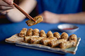 Hand of man behind table eating spring roll with chopsticks. Tasty food in Vietnam..