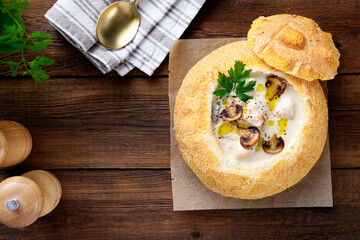 Cream soup with chicken and mushrooms, beautifully served in a bun. Wooden background, top view