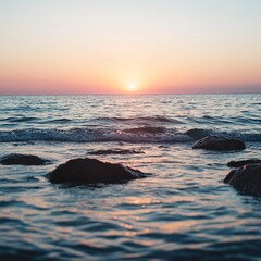 Obraz premium Ocean waves softly break against the rocks under a colorful sky at sunset, evoking a sense of peace.