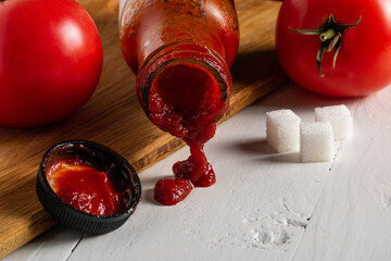 Ketchup in a glass bottle and sugar cubes nearby. Added sugar in products.