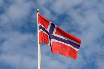 Norwegian flag proudly waving under a bright blue sky with fluffy clouds during a sunny day in Norway
