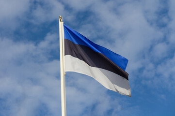 Waving proudly, the Estonian flag flutters against a backdrop of blue skies and soft clouds, symbolizing national pride and unity