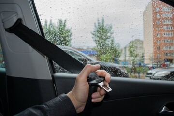 The driver's hand pulls out the seat belt before driving against the background of the yard and drops on the glass