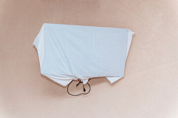 Covered wall-mounted TV wrapped in white fabric with a visible power cord hanging below, attached...
