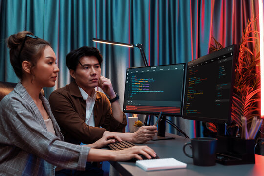 IT developers discussing with point to intelligent website development coder system running data online two screens information technology at neon light room at modern office. Infobahn.