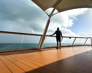 Lone silhouette stands by a railing looking out to sea on a sunny yet cloudy day, with space for text