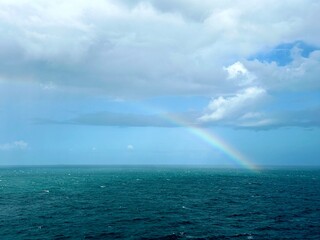 A clear rainbow in the middle of the ocean breaking through the clouds into the sea