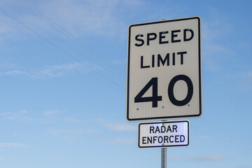 Radar enforced speed limit signage against blue sky and clouds.