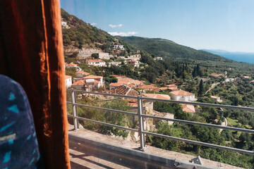 Small village in the mountains. Travel background. Beautiful scenic views. Exploring Albania by public transport. View from a bus window. Coach window landscape. Forest hill cliff.