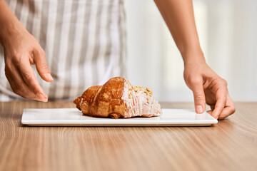 female hand holding fresh handmade croissant on white plate
