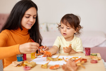 Cute little girl and mom spending good time painting hands and autumn yellow leaves together