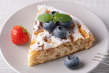 Delicious slice of cake topped with fresh blueberries and a strawberry on a light wooden table