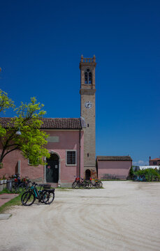 Square of a small Italian village. Bell tower with clock and bicycles parked nearby. Vertical image. Lio Piccolo, Italy, 18 May 2024