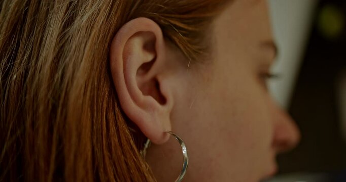 Close Up video of a young woman with auburn hair and silver hoop earrings.