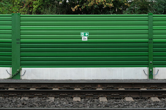 Gr&uuml;ne L&auml;rmschutzwand an Bahnstrecke mit Schild Notausgang 50m - Stockfoto