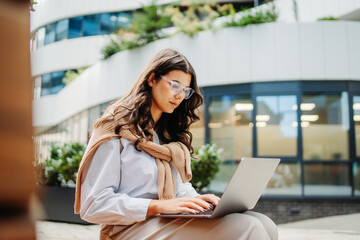 Young businesswoman working on laptop outside of modern business building