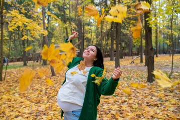 Happy 42 year old pregnant woman throws yellow leaves up, walks in autumn park. Pregnancy after 40,...